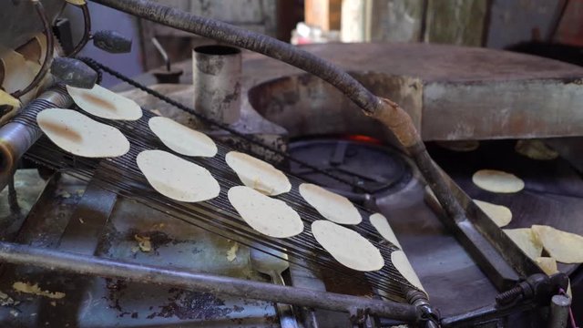 Freshly stamped corn tortillas falling from the cutter and going onto the griddle part of the machine.