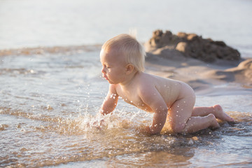Baby boy, playing on the beach in the water, smiling