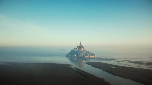 Atmospheric cinematic aerial shot of foggy sunrise Mont Saint Michel on high tide, famous island fortress in Normandy.