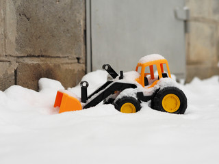 The toy tractor in snow. Cleaning of snow after a blizzard. Children's game in the winter. The...