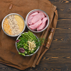 Natural raw ingredients for healthy pet food ingredients with turkey, groats, greens and sprouts in individual bowls on brown wooden background. Flat lay.