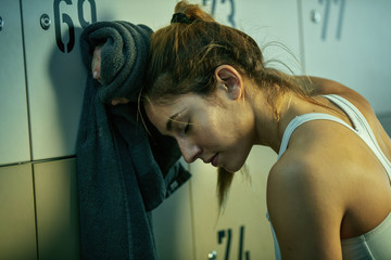 Exhausted athletic woman resting in locker room with her eyes closed.