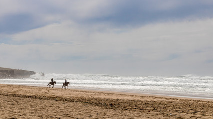 Fototapeta na wymiar Horseback riding on Guincho Beach. Relaxing calm scene of two isolated people enjoying a beautiful day on holiday