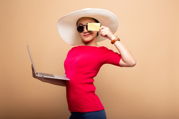 Woman wearing hat and sunglasses use laptop and credit card isolated on background