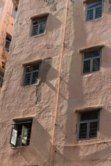 Windows of an old concreted apartment building, painted a light pink salmon color. Hong Kong.