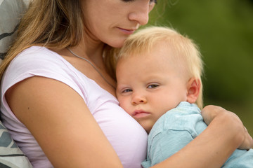 Young mother, holding her cute baby boy outdoor, cuddle him, kissing and huging, sitting outdoor on the porch
