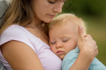 Young mother, holding her cute baby boy outdoor, cuddle him, kissing and huging, sitting outdoor on the porch