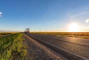 A truck travels along an empty long straight road in the New South Wales countryside on a blue sky...