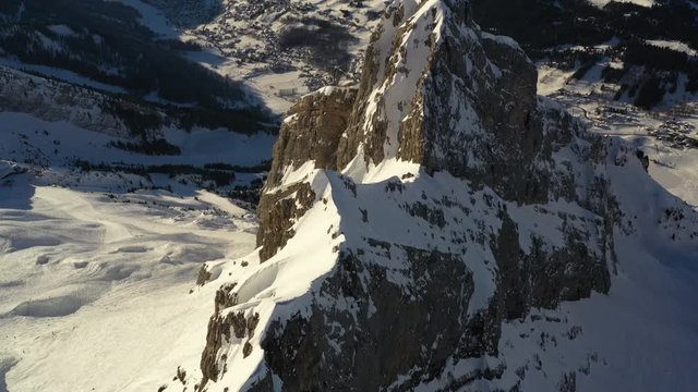 Aerial view flyng over a mountain ridge with mountains in the background, while tilting down to look at the ridge from above in the French Alps in winter, near La Clusaz.