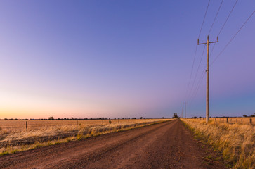 A long straight dirt road through rural farmlands extends to a vanishing point at the horizon...