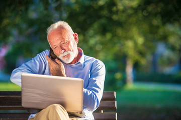 Fototapeta premium Business correspondence. Focused mature businessman using laptop while sitting in park