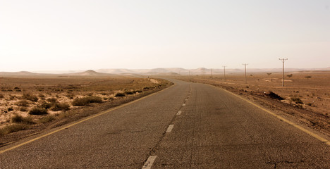 Highway through scenic desert of Jordan. High voltage powerlines along asphalt road in arid valley. Early morning in wilderness after sunrise. Electric power poles. Horizontal.