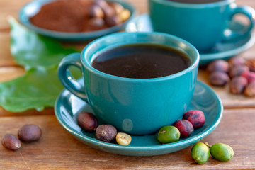 Cup with black coffee served outside with raw green, mature red and roasted coffee beans, decorated with green leaves from coffee plant