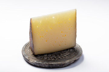Piece of Spanish hard scheep milk cheese Manchego on grey stone plate isolated close up