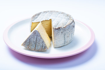 Round mature French Tomme cheese with cutted piece close up isolated