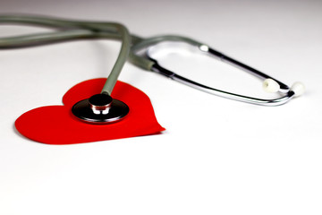 Medical stethoscope on the white background with red paper heart. The concept of Cardiologycal research.  