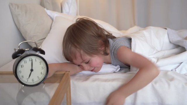 Sweet kid sleeping with alarm clock near his head.
