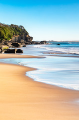 Vertical portrait format photo of golden sands and a shoreline on a secluded beach in morning afternoon light.  Jenny Dixon Beach, New South Wales, Australia..