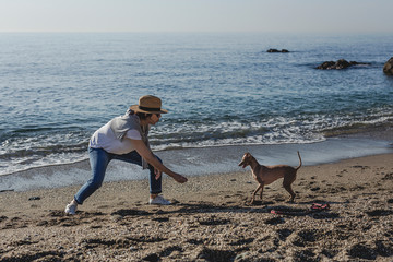 Beautiful brunette woman playing with dog on the beach