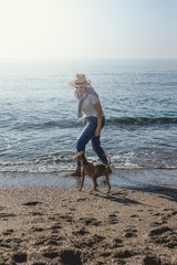 Beautiful brunette woman playing with dog on the beach