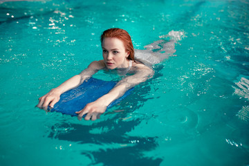 Beautiful young redhead Caucasian girl swims in the indoor swimming pool. Healthy lifestyle.