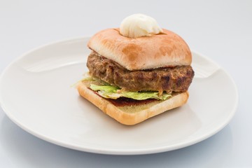 cheeseburger with beef cutlet, bacon, tomatoes and cheese slices, seasoned with sauce and green salad for a restaurant menu on a white isolated background