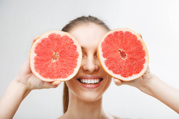 Portrait of young woman with clean skin holding two pieces of grapefruit