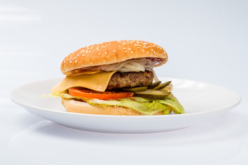 cheeseburger with beef cutlet, bacon, tomatoes and cheese slices, seasoned with sauce and green salad for a restaurant menu on a white isolated background