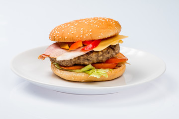 cheeseburger with beef cutlet, bacon, tomatoes and cheese slices, seasoned with sauce and green salad for a restaurant menu on a white isolated background