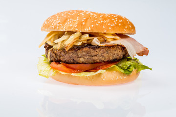 cheeseburger with beef cutlet, bacon, tomatoes and cheese slices, seasoned with sauce and green salad for a restaurant menu on a white isolated background