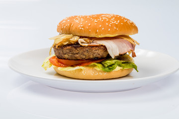 cheeseburger with beef cutlet, bacon, tomatoes and cheese slices, seasoned with sauce and green salad for a restaurant menu on a white isolated background