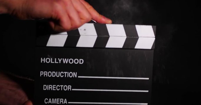 Hands holding blank Hollywood clapperboard closed sharply to release dust from edges.