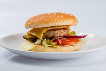 cheeseburger with beef cutlet, bacon, tomatoes and cheese slices, seasoned with sauce and green salad for a restaurant menu on a white isolated background