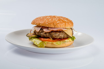 cheeseburger with beef cutlet, bacon, tomatoes and cheese slices, seasoned with sauce and green salad for a restaurant menu on a white isolated background