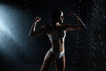 Fototapeta na wymiar Beautiful athletic caucasian girl with a perfect figure is standing under the water. Fitness woman in a spray of water. Sports freshness