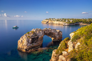 Es Pontas in Mallorca, natural arch in the Mediterranean sea at sunrise with a boat anchored nearby...