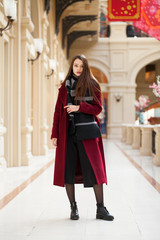 Beautiful girl in stylish in a long burgundy coat, indoor shop