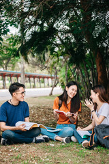 A group of young or teen Asian student in university smiling and reading the book and look at the tablet or laptop computer in summer holiday.