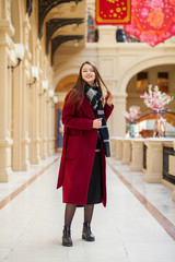 Fototapeta premium Beautiful girl in stylish in a long burgundy coat, indoor shop