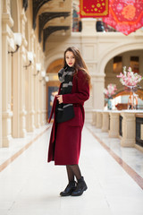 Fototapeta na wymiar Beautiful girl in stylish in a long burgundy coat, indoor shop