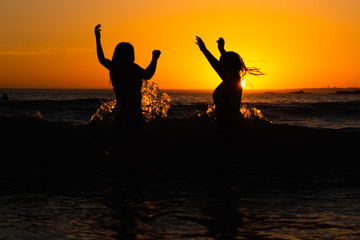 Girls jump with wave at sunset
