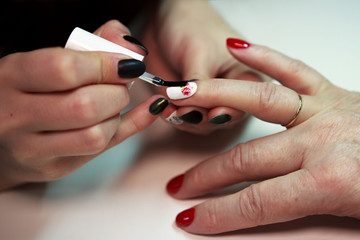 master glues a decal with a rose on the nails on a red and white lacquer manicure. reporting shooting.