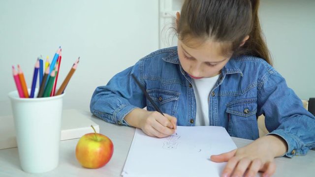 school girl in jeans wear drawing with colored pencil and eating apple
