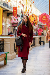 Fototapeta premium Beautiful girl in stylish in a long burgundy coat, indoor shop