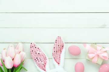 Table top view shot of decorations Happy Easter holiday background concept.Flat lay bunny eggs with pink tulip and variety decor for season and gift box on modern rustic white wooden.Mock up design.
