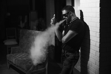 Men with beard vaping in sunglasses at home. Black and white photography