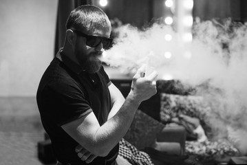 Men with beard vaping in sunglasses at home. Black and white photography