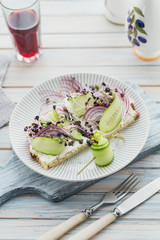 Healthy vegetarian bruschettas with bread, micro greens, cheese, cucumbers and red onion on light...