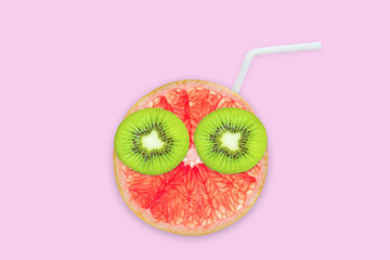 Fruit creative face with slices of grapefruit and kiwi, drinking straw on pink background, fruit juice and summer concept