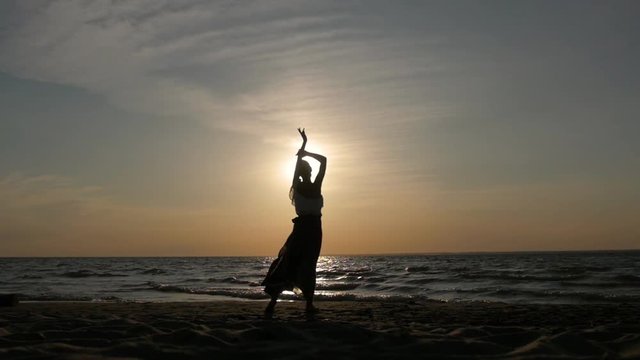 silhouette of a woman at sunset dancing on the beach. flying skirt